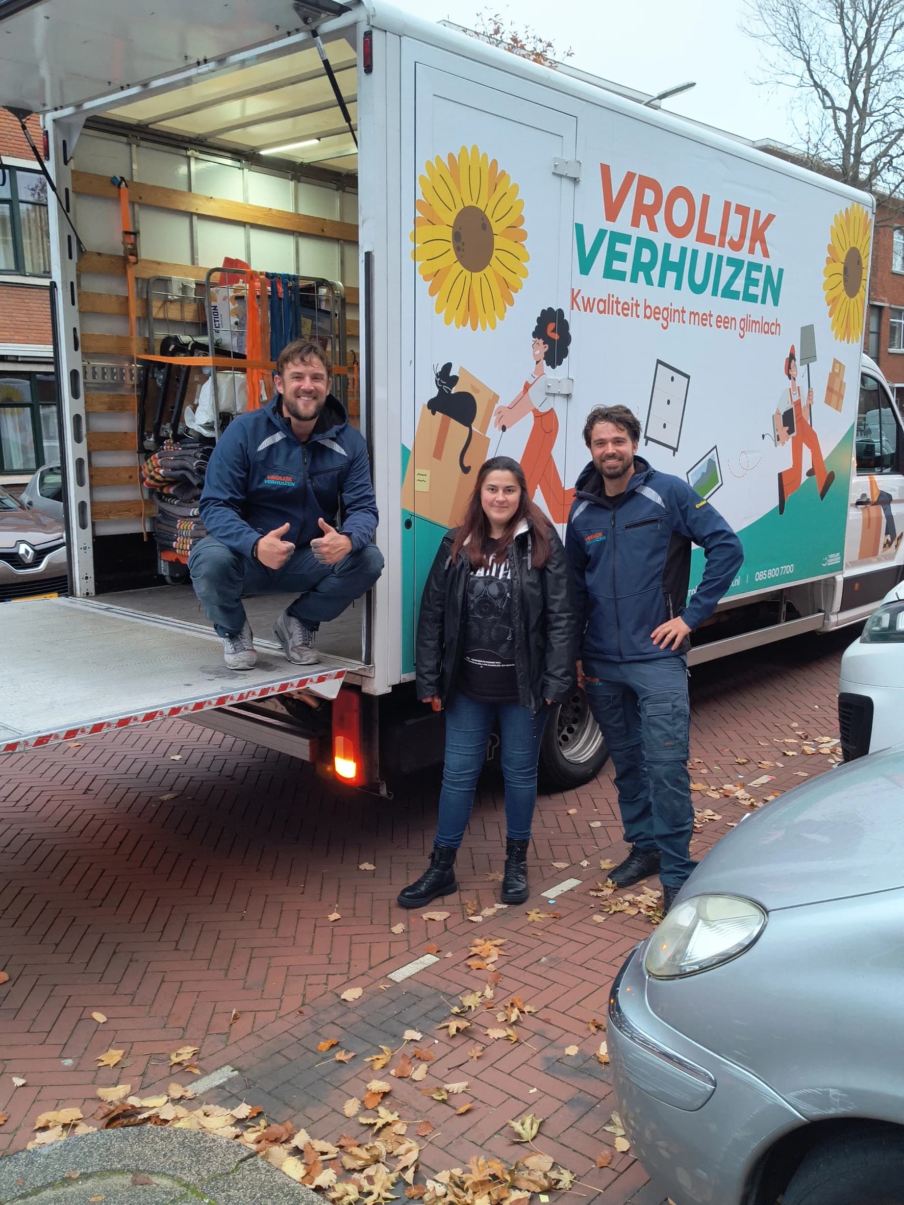 Twee Vrolijk Verhuizen crewleden met een blije klant bij de laadklep